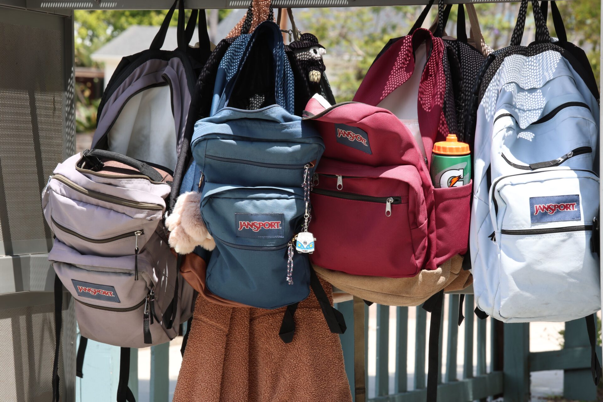 A line of colorful JanSport school backpacks hanging outdoors, ready for the back to school season.