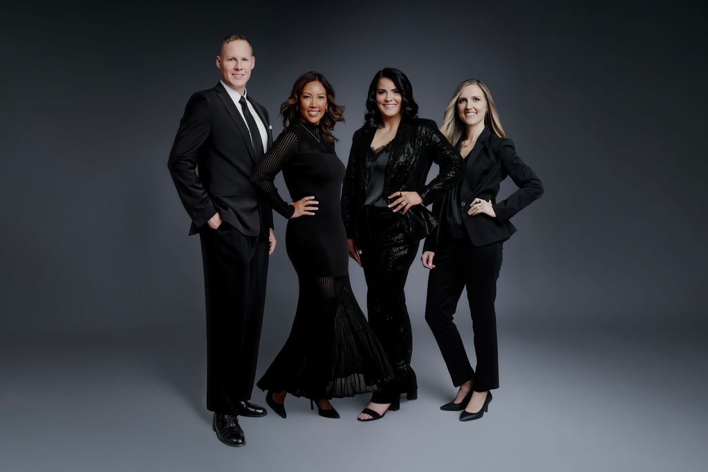 A professional dentist team of four wearing elegant black attire posing together in a studio setting.
