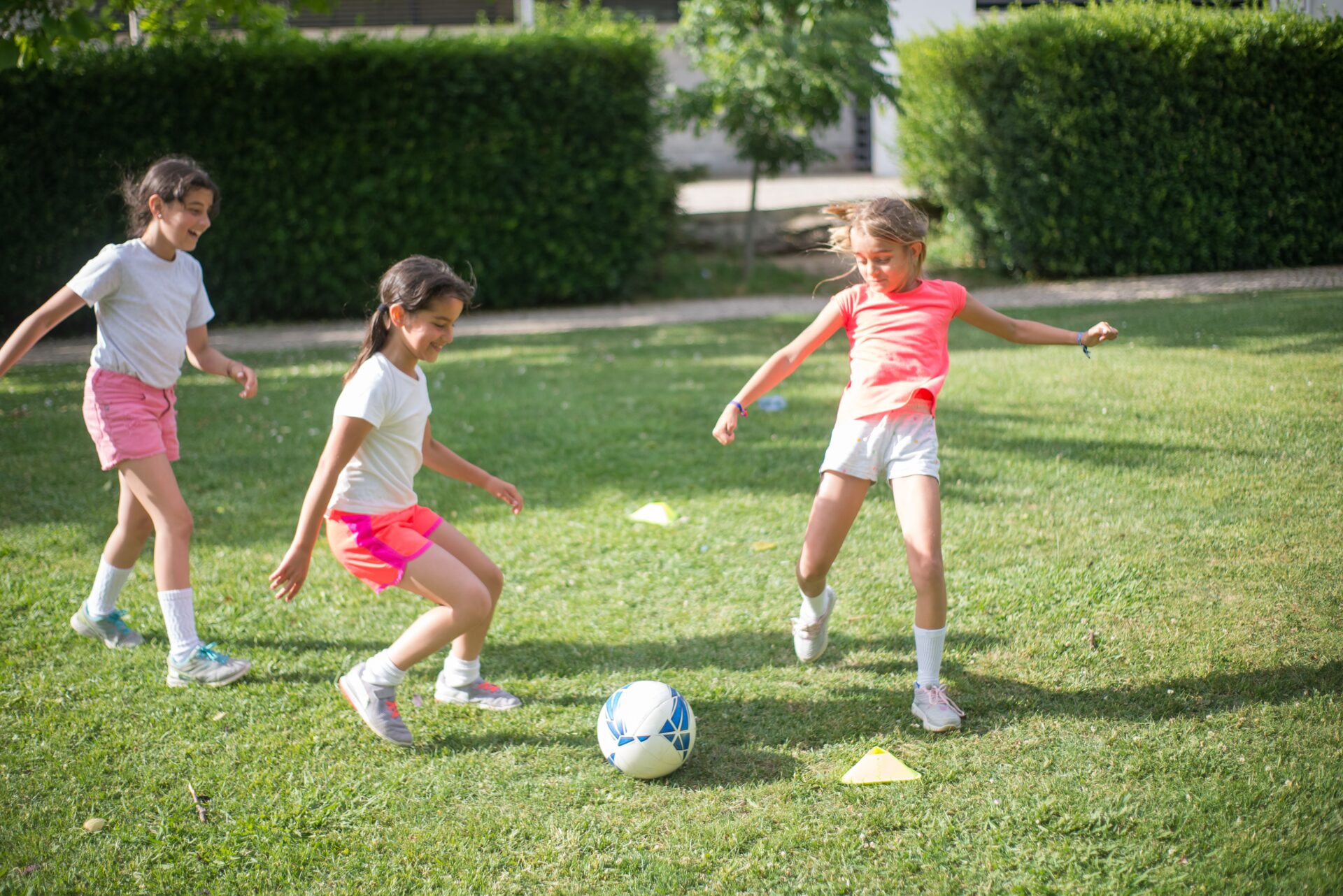 Three young girls playing a game of soccer together on a grassy field during outdoor kids activities.