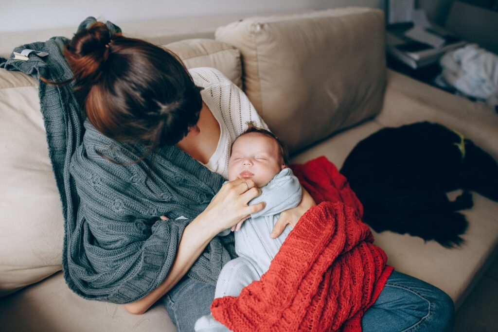 : Postpartum mother holding her newborn baby while resting together on a couch